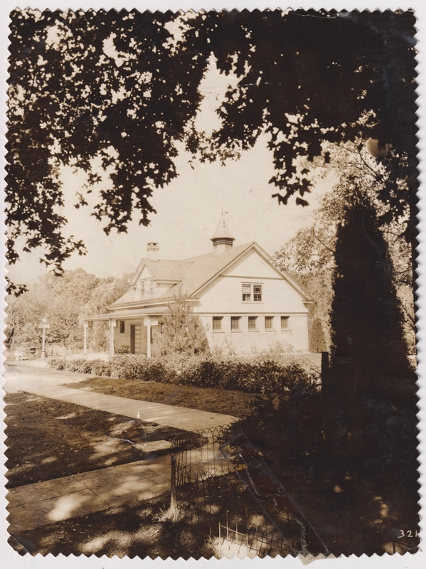 A black-and-white photograph of the Carriage House building on the Haddonfield Bancroft campus. It is a small light-colored building with a cupola on the roof, surrounded by bushes and trees.